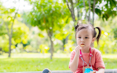 Cute little asian boy eating chips or potato wafers at park. Copy space.