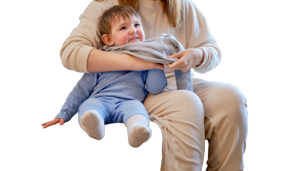 Child is dressed in warm winter clothes for a walk outside, isolated on white background. Woman mother puts clothes on toddler baby boy for cold weather. Kid age one year five months