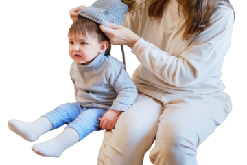 Child is dressed in warm winter clothes for a walk outside, isolated on white background. Woman mother puts clothes on toddler baby boy for cold weather. Kid age one year five months