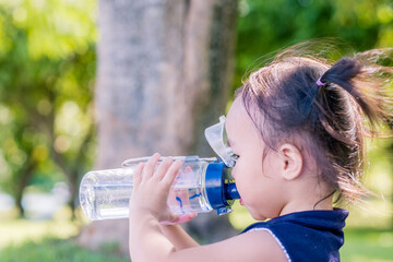 Little asian girl drinking water in garden park. Summer day. Copy space.	