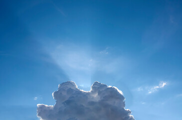 Blue sky with a fluffy cloud and sunbeams radiating from behind it - 754171883