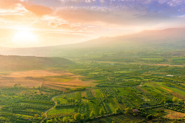 scenic rustic landscape with green hills and farms in a mountain valley during colorful cloudy sunset