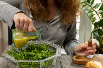 A woman pours olive oil over rocket leaves and quinoa salad. Fresh homemade salad with arugula,...