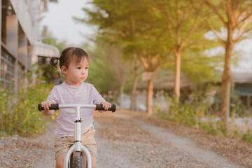 Little girl learns to keep balance while riding a bicycle at park. Copy Space.