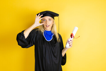 Beautiful blonde young woman wearing graduation cap and ceremony robe Trying to open eyes with...