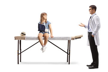 Obraz premium Little girl with a broken arm sitting on a physical therapy bed and listening to a male doctor