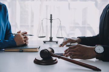 Justice and Law concept. Legal counsel presents to the client a signed contract with gavel and legal law or legal having team meeting at law firm in background