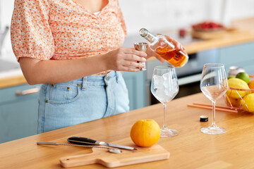 drinks and people concept - close up of woman pouring liquor from glass bottle to jigger and making cocktail at home kitchen - 754222034