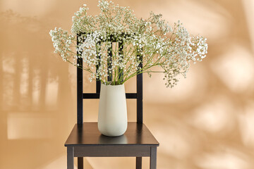 home decor and design concept - close up of gypsophila flowers in vase on vintage chair over beige background - 754224460