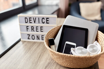 digital detox and technology concept - close up of device free zone words on light box and different gadgets in wicker basket on table at home - 754225693