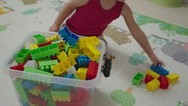 Toddler baby collects toys in a box. Child himself cleans up toys in the nursery after the game.