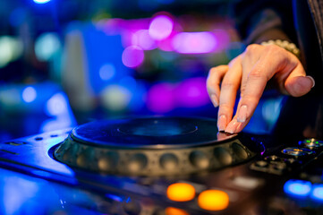 A skilled DJ’s hand deftly manipulates a turntable amidst vibrant club lights. The close-up view...