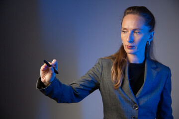 Business woman holding a light pencil in her right hand on a gray background. Focus on the hand. Close-up. Blue color correction
