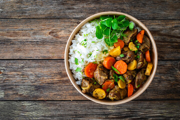 Takeaway food - roast pork with carrots and celeriac in sauce with white rice in lunch box on wooden table
