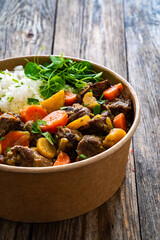 Takeaway food - roast pork with carrots and celeriac in sauce with white rice in lunch box on wooden table
