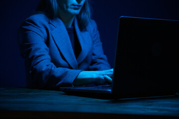 Business woman working on a laptop in the dark and illuminated by the screen. No face. Focus on...