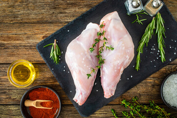 Raw rabbit thighs on cutting board with seasonings on wooden table
