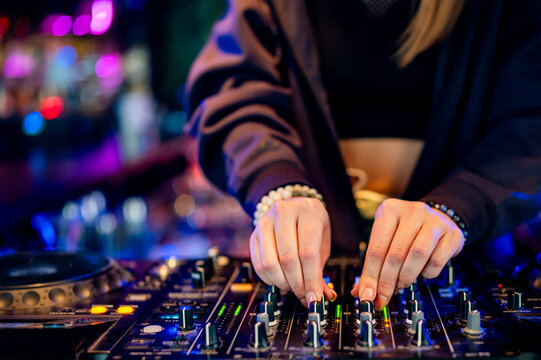 A DJ deftly adjusts knobs on a vibrant console, immersed in the pulsating rhythm of the nightlife. Colorful lights illuminate the scene, creating an electric atmosphere