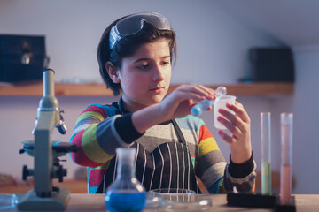 A cute young chemist in a home research laboratory wearing safety glasses is intently conducting...