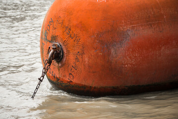 Nahaufnahme eines orangenen Bootsfender befestigt mit einer Eisenkette in der Themse, London,...