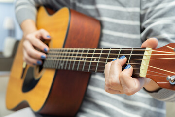 girl playing acoustic guitar at home, closeup