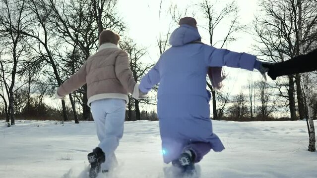 Friends holding hands running through the snow on a sunny day.