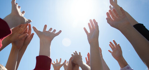 Hands reach out to the sun against the backdrop of a bright blue sky