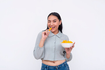Joyful young Asian woman winking with a playful gesture while eating cheese puffs, isolated on a...