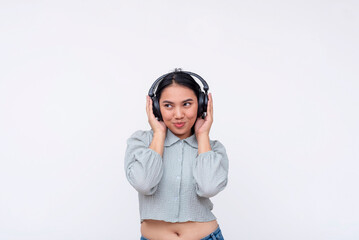 A cheerful young Asian woman with wireless headphones enjoying a podcast or streaming music, standing against a white background.