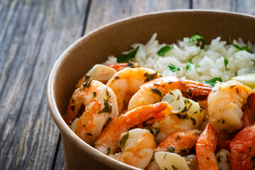 Fried shrimps with boiled white rice and lime in lunch box to go on wooden table

