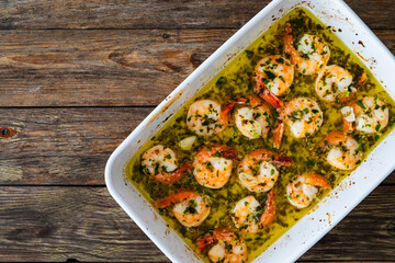 Fried shrimps with parsley and garlic in olive oil in cooking pan on wooden table
