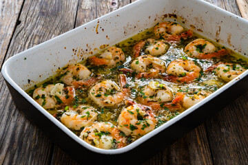 Fried shrimps with parsley and garlic in olive oil in cooking pan on wooden table
