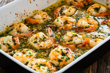 Fried shrimps with parsley and garlic in olive oil in cooking pan on wooden table
