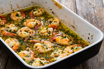 Fried shrimps with parsley and garlic in olive oil in cooking pan on wooden table
