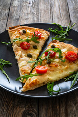 Roman pinsa slices with mozzarella cheese, capers, arugula and garlic on wooden table

