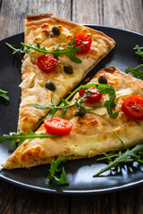 Roman pinsa slices with mozzarella cheese, capers, arugula and garlic on wooden table

