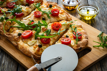 Roman pinsa with mozzarella cheese, capers, arugula and garlic on wooden table
