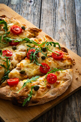 Roman pinsa with mozzarella cheese, capers, arugula and garlic on wooden table
