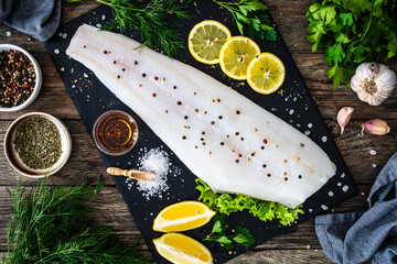 Fresh raw halibut fillet with lemon and dill on black stony  cutting board on wooden table
