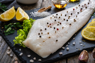 Fresh raw halibut fillet with lemon and dill on black stony  cutting board on wooden table
