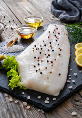 Fresh raw halibut fillet with lemon and dill on black stony  cutting board on wooden table
