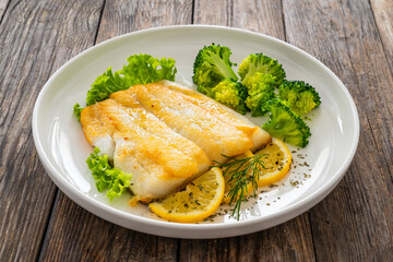 Seared halibut fillet, sliced lemon and boiled broccoli on wooden table
