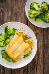 Seared halibut fillet, sliced lemon and boiled broccoli on wooden table
