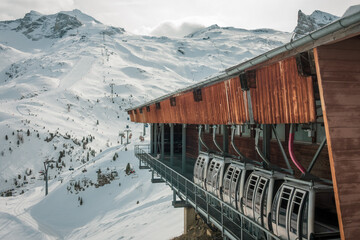 Parked ski cabins, gondolas in a wooden big house, and a ski piste in distance - Powered by Adobe
