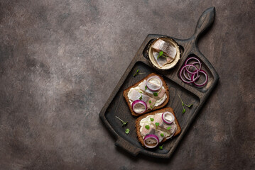 Sandwiches with herring. Rye bread with herring, red onion and microgreens on a dark background. Top view, flat lay, copy space. - 754287859