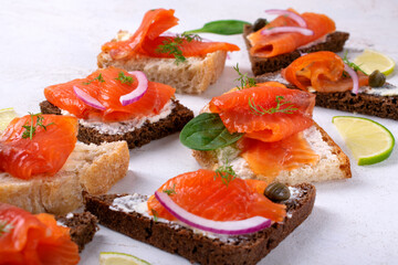 Bruschetta set with smoked trout slices, cream cheese and capers on wheat and rye bread. Tasty appetizers on white