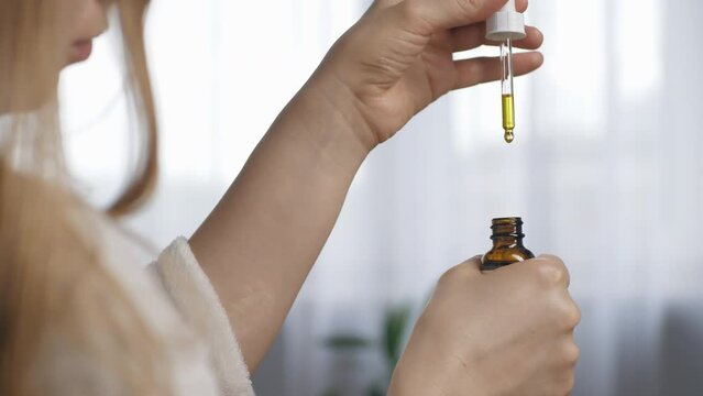 A woman is holding a dropper that drips facial oil into her palm. Close up. Normal skin care, cosmetic oil, serum, pure natural.