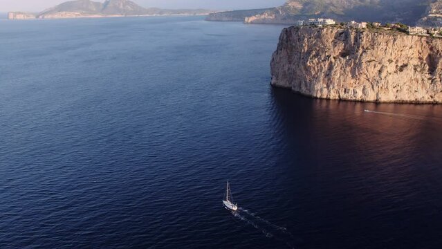 Cinematic aerial drone shot of epic Mallorca cliff surrounded endless blue sea or ocean. Luxury yacht sailing in open water. Perfect summer vacation and holiday travel destination. 