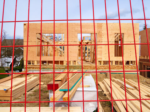 Wooden frame and walls of new house behind the red fence grid
