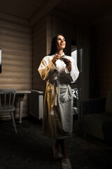 Young woman in a white bathrobe drinks espresso coffee in a wooden hotel room. Hotel holiday...
